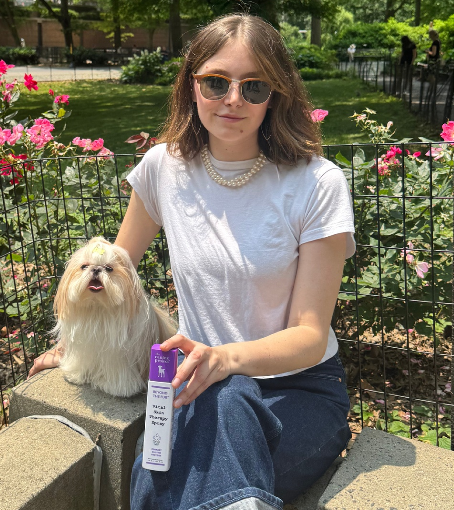 Woman holding a product package with a small dog in a park setting